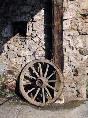 An old wagon wheel leans against a stone barn in a village in the Picos de Europa, Spain